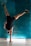 A person is performing a handstand against a textured teal wall, with a visible focus on balance and strength. The athlete is wearing athletic shoes and dark sportswear, with a small horizontal light fixture on the floor beneath.