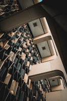 An interior architectural structure features a complex wall design with three-dimensional geometric patterns. The ceiling has a grid-like structure with recessed lights, and the composition creates an abstract, futuristic appearance.