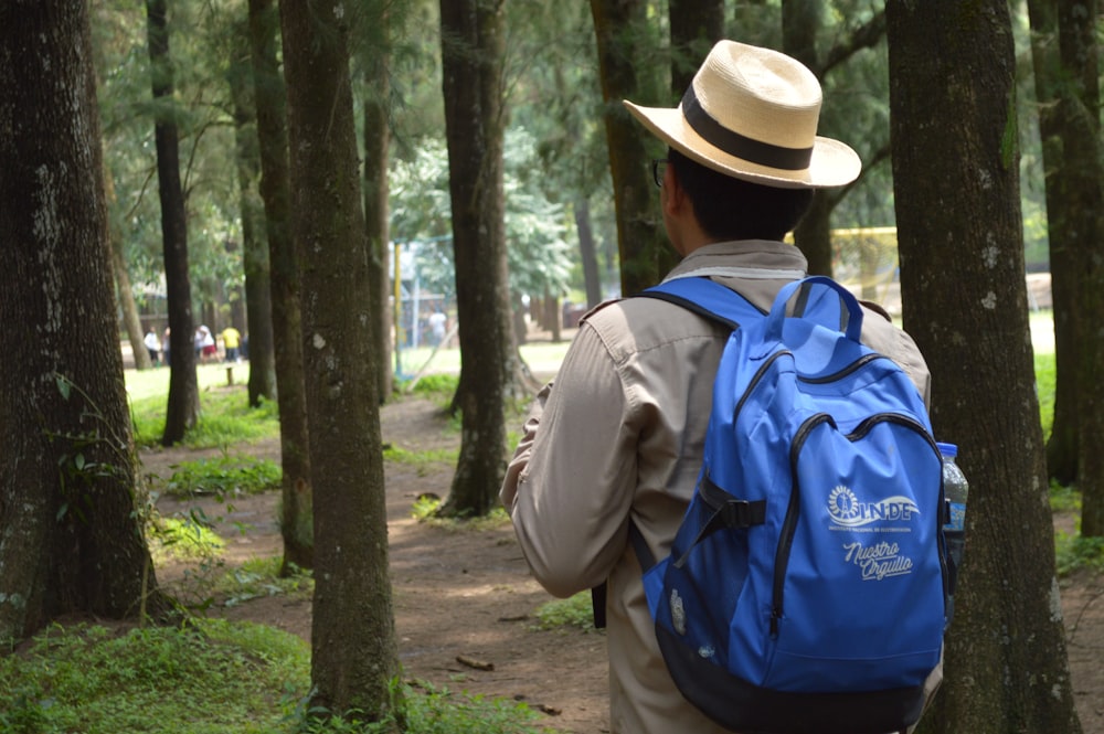 man in blue and black backpack standing near green trees during daytime