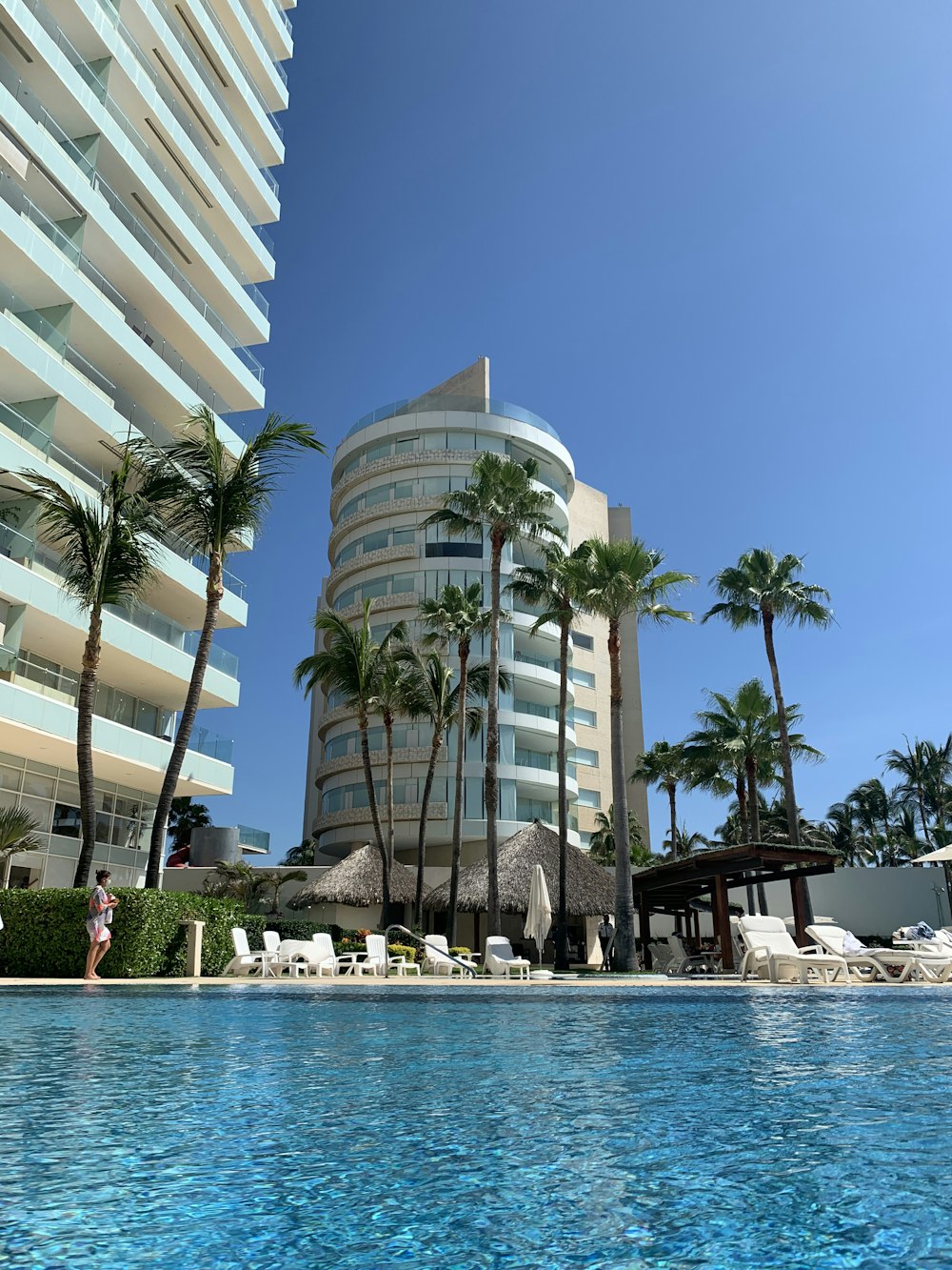 white concrete building near palm trees and swimming pool during daytime