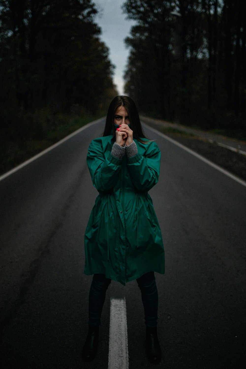 woman in green coat standing on road during daytime
