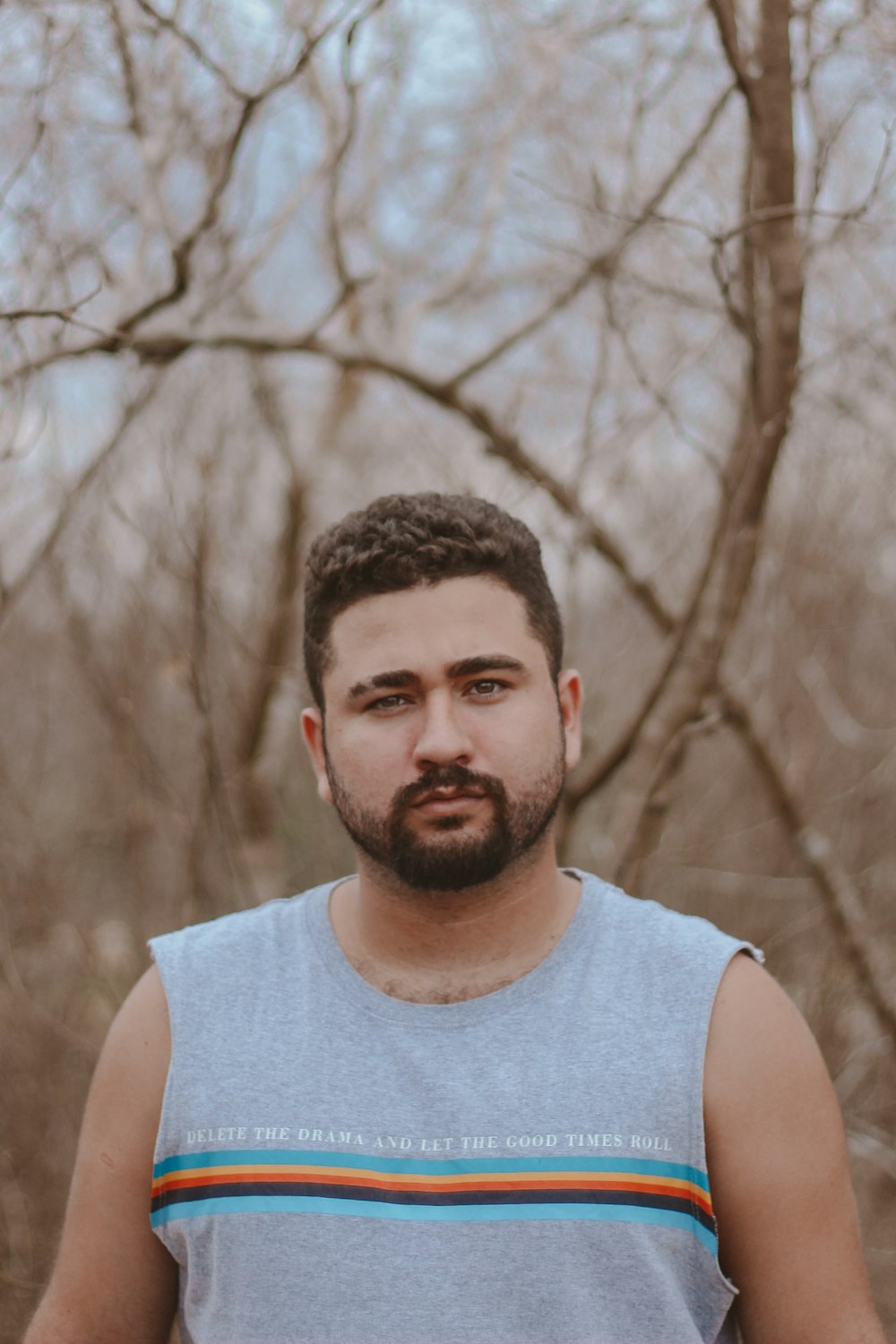 man in gray tank top standing near brown trees during daytime