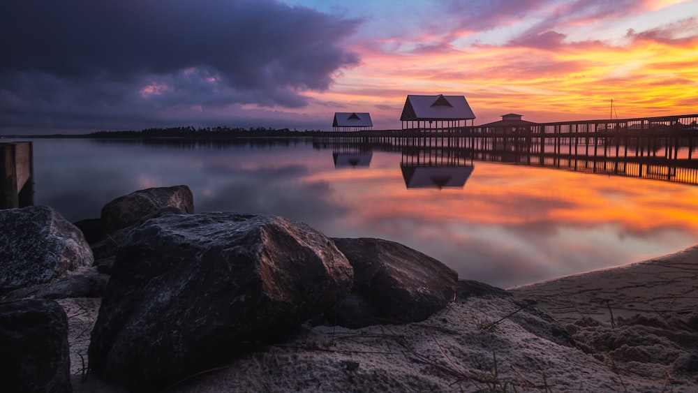 brown wooden house on rocky shore near body of water during sunset