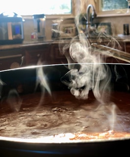 A steaming pot on the stove with aromatic steam rising, surrounded by jars of homemade sauces.
