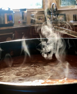 A steaming pot of soup simmering on a kitchen stove with herbs nearby.