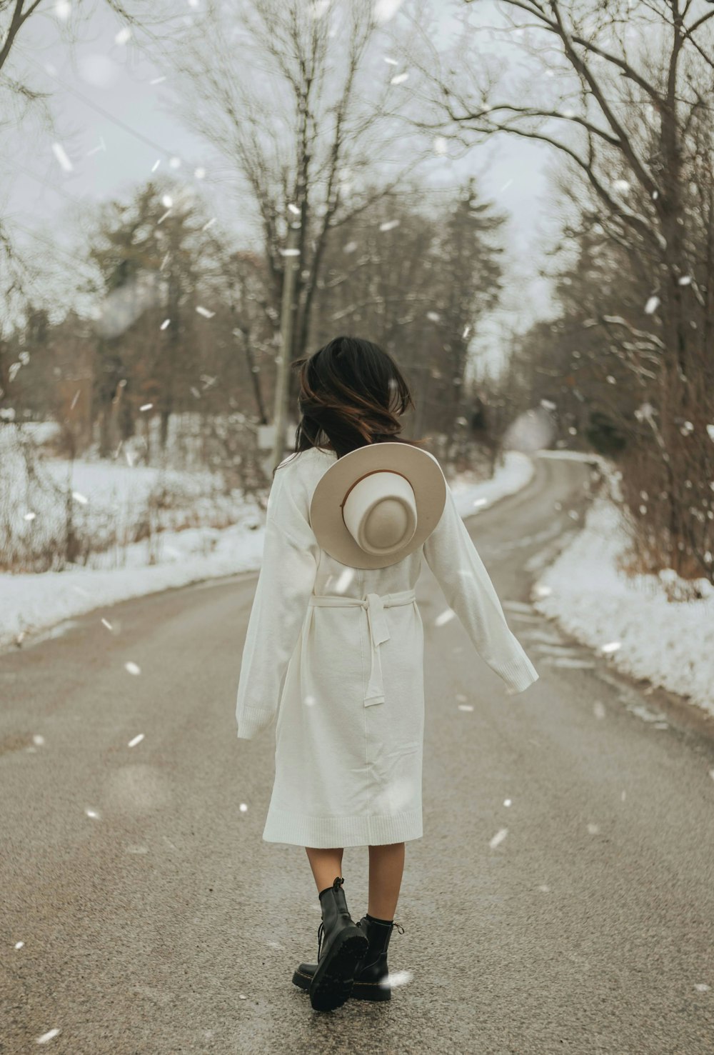 woman in white coat standing on road covered with snow during daytime