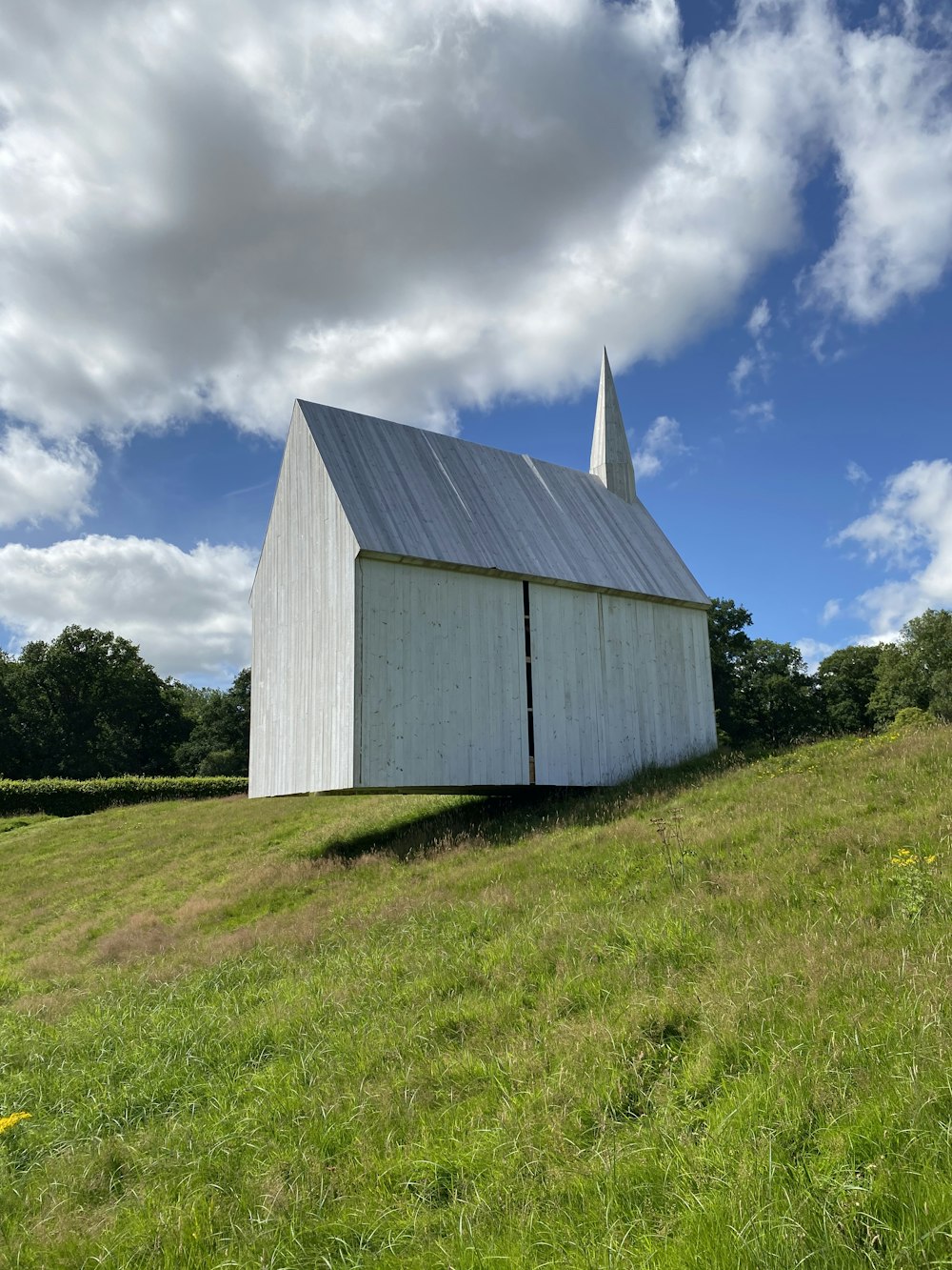 white wooden barn on green grass field under blue sky and white clouds during daytime