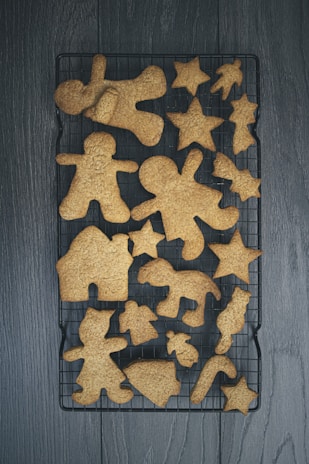 Various gingerbread cookies are arranged on a black cooling rack. The cookies come in different shapes, including stars, hearts, and gingerbread people.