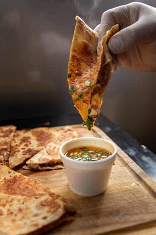 Hands folding a quesadilla filled with gooey birria cheese and meat over a sizzling hot griddle.