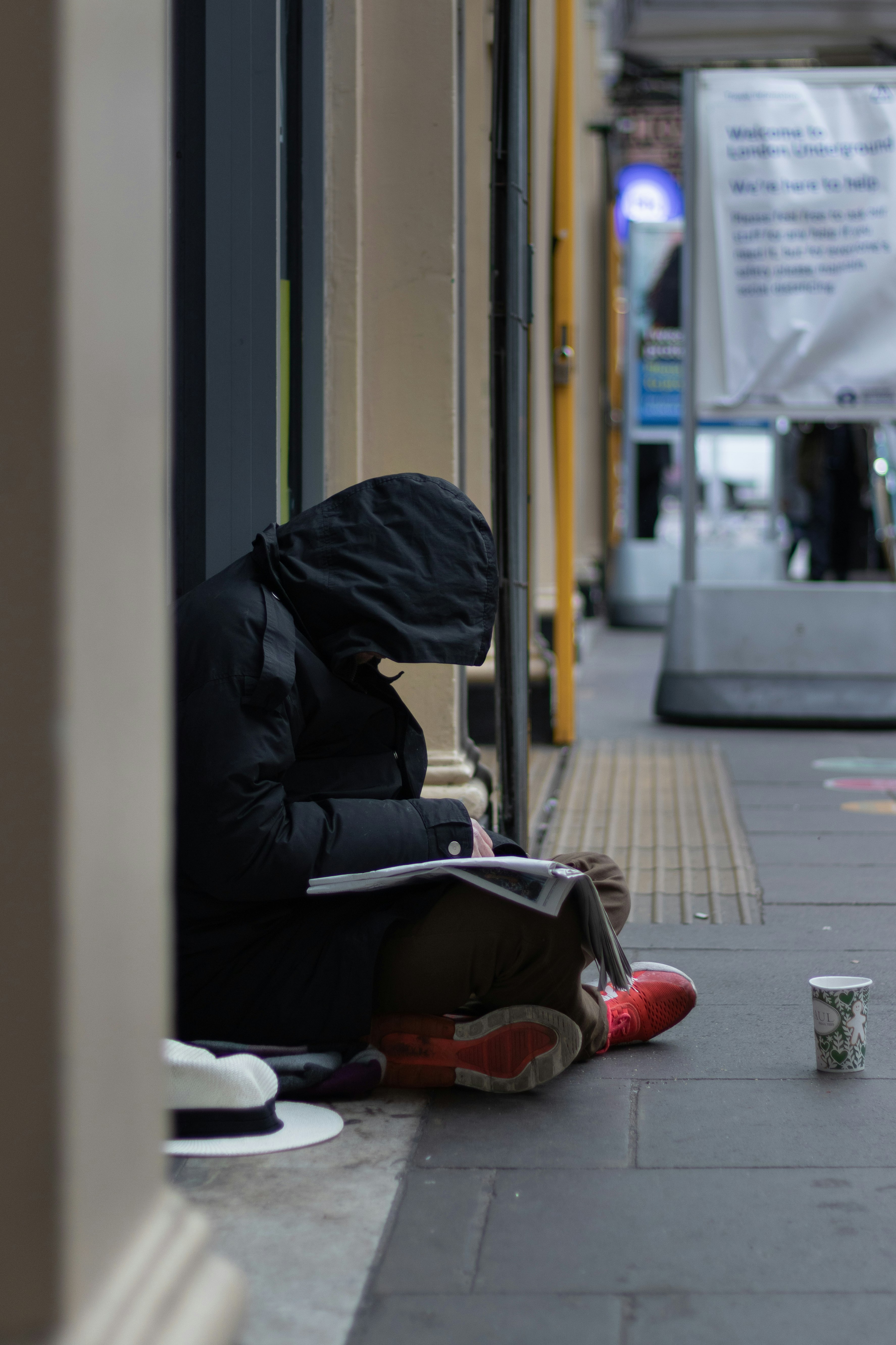 person in black hoodie sitting on sidewalk during daytime