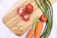 A wooden chopping board with fresh vegetables and a knife on a kitchen countertop.
