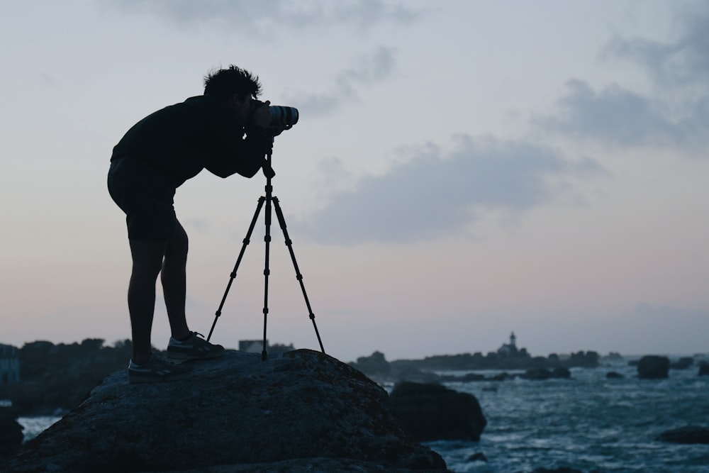 silhouette of man standing on rock near body of water during daytime