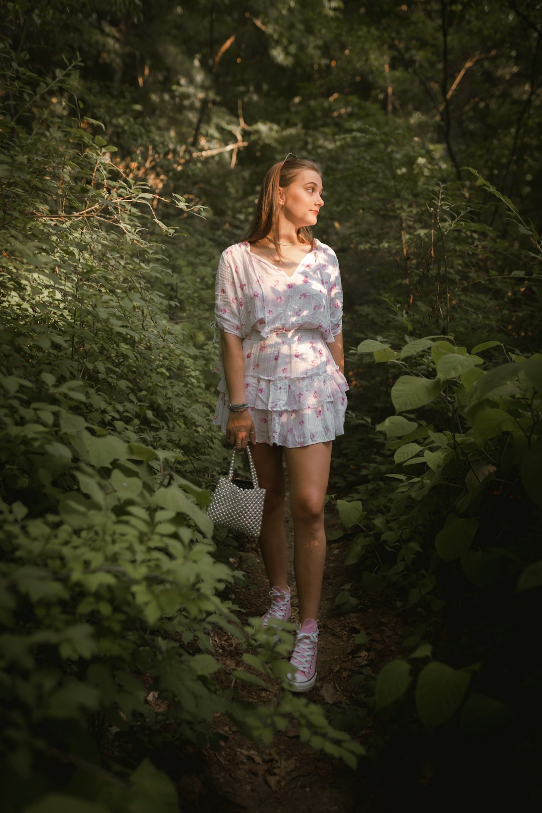 woman in white and pink floral dress standing beside green plants