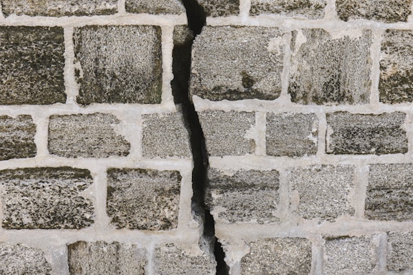 A visible crack in a wall representing the breaking point of tolerance against systemic harm