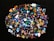 A collection of colorful, polished gemstones scattered on a dark surface. The stones have a variety of shapes, including triangles and ovals, with complex patterns and vibrant hues like blues, reds, yellows, and greens.