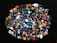 A collection of colorful, polished gemstones scattered on a dark surface. The stones have a variety of shapes, including triangles and ovals, with complex patterns and vibrant hues like blues, reds, yellows, and greens.