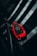 A red car key with a luxury brand logo is resting on a reflective dark surface, likely a windshield. The key features multiple buttons for locking, unlocking, and opening the trunk.