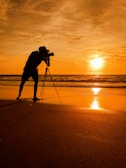 Sunset over a serene beach with a lone figure capturing the horizon on camera.