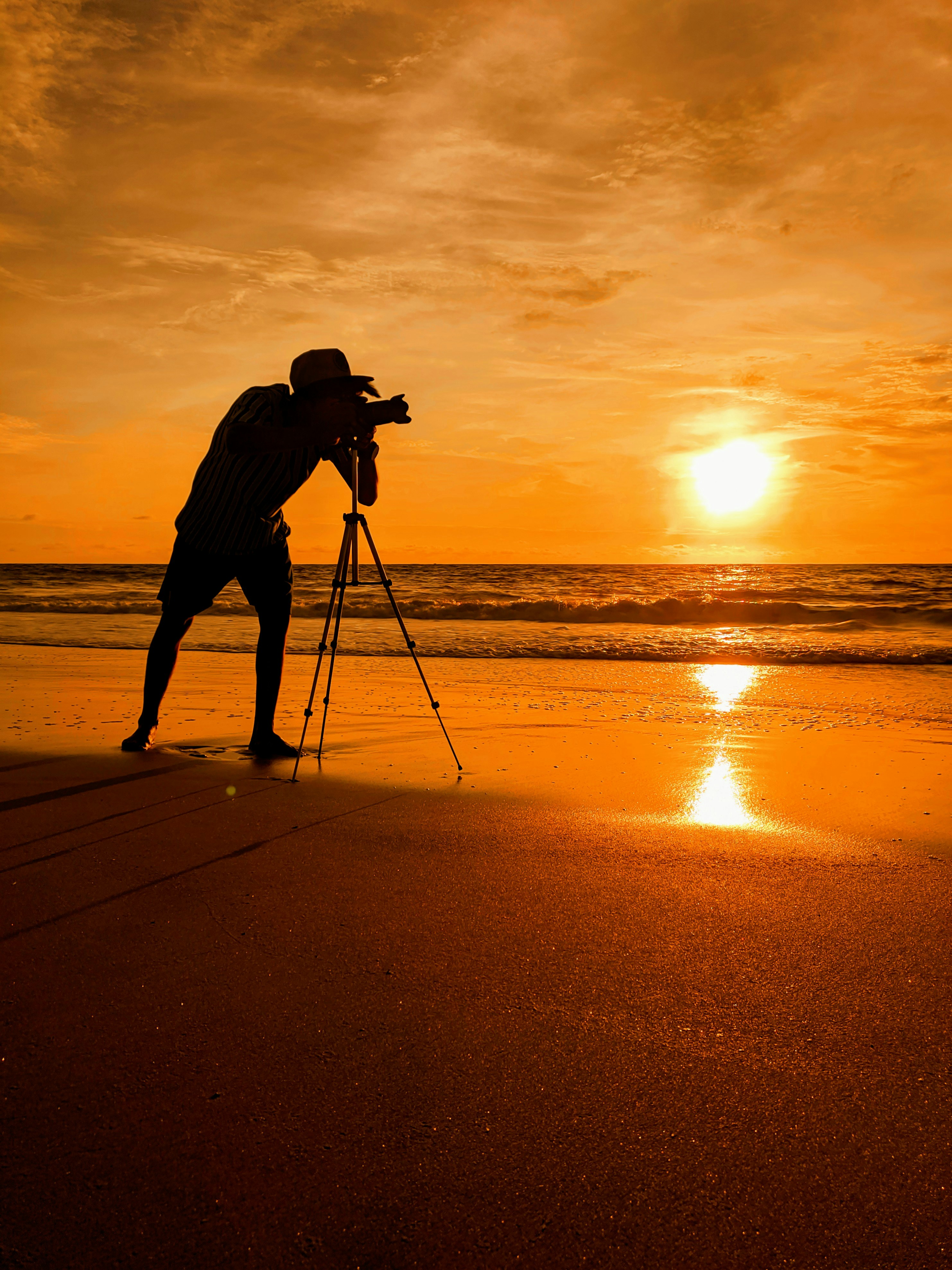 silhouette of man holding camera on tripod on beach during sunset