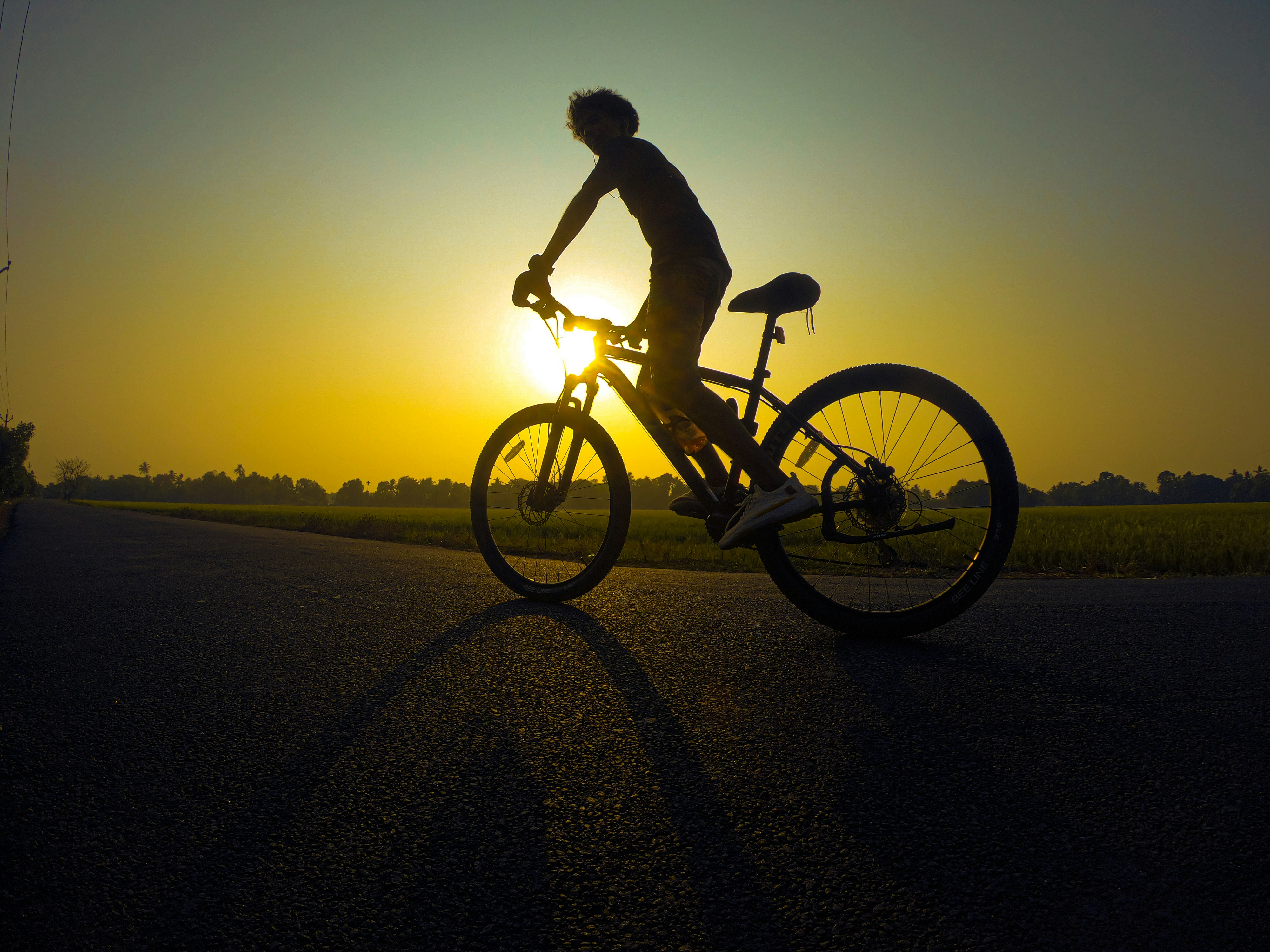 man in black jacket riding bicycle on gray sand during sunset