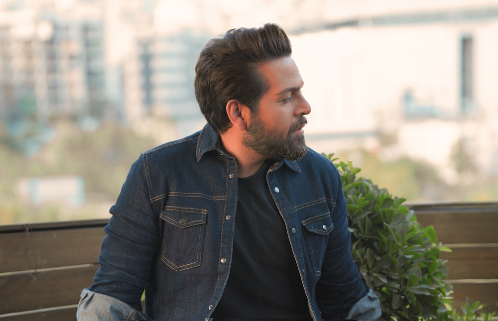 man in blue denim jacket sitting on bench during daytime