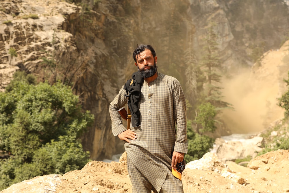 man in gray and white long sleeve shirt standing on brown rock during daytime