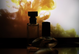 Two perfume bottles are silhouetted against a vibrant, swirling background of yellow and orange hues. The lighting casts a dramatic effect, highlighting the contours and elegance of the glass bottles.