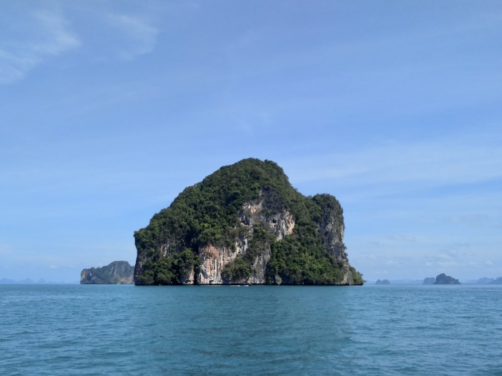 formación rocosa verde y marrón en el mar azul bajo el cielo azul durante el día