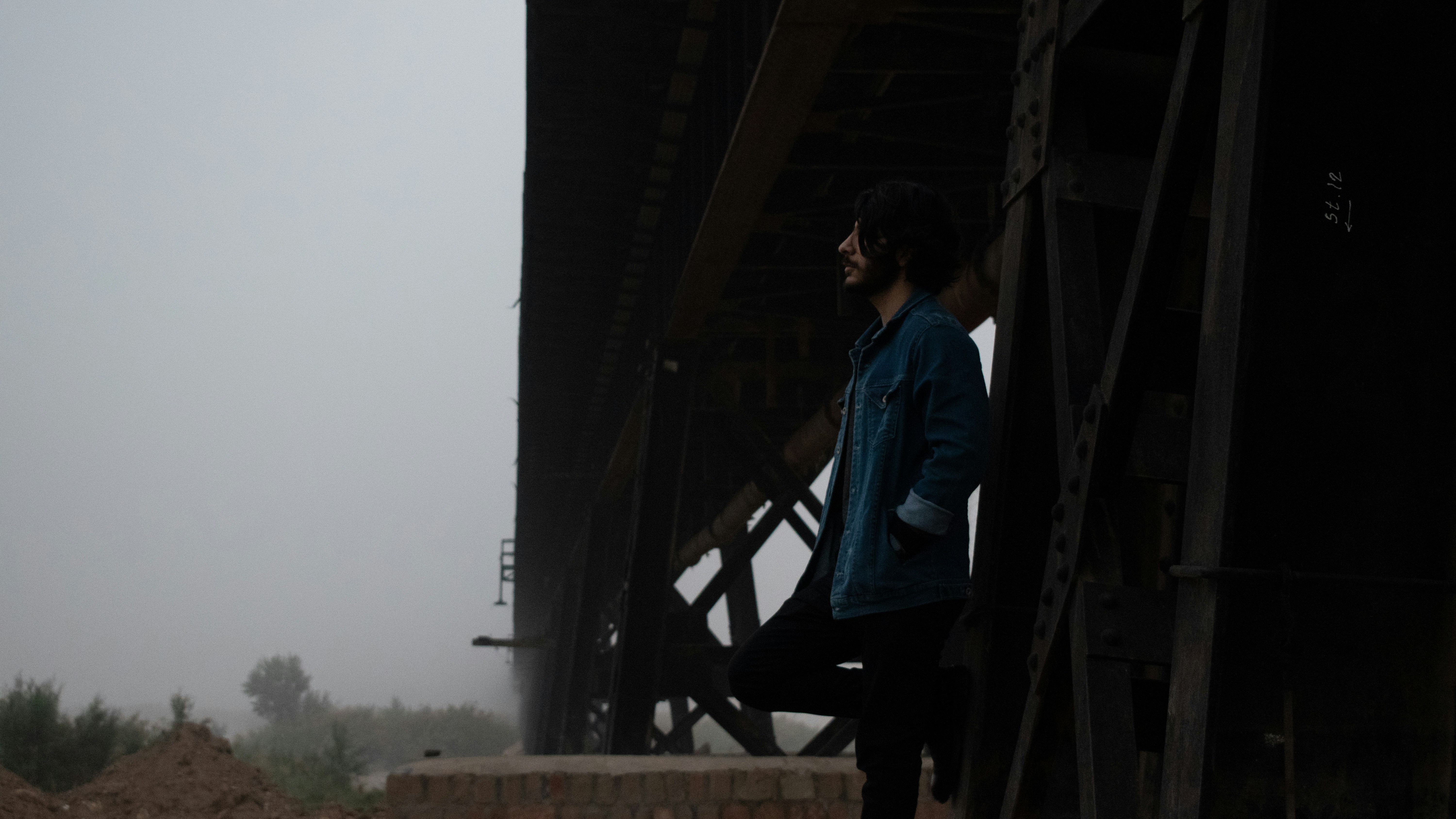 man in blue dress shirt and black pants standing on brown wooden bridge during daytime