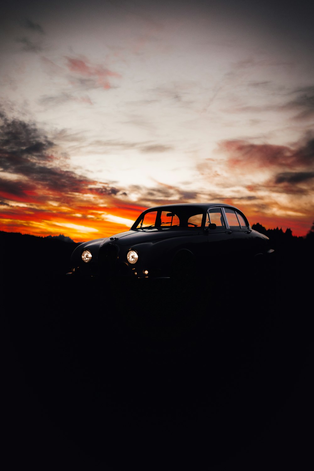 um carro estacionado em um campo com um pôr do sol ao fundo