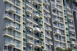 A modern high-rise building with multiple balconies and large glass windows. The architecture features a grid pattern with alternating light and dark panels, creating a sleek and contemporary look.