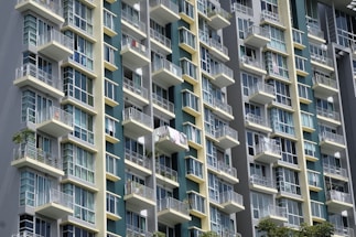 A modern high-rise building with multiple balconies and large glass windows. The architecture features a grid pattern with alternating light and dark panels, creating a sleek and contemporary look.