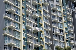 A modern high-rise building with multiple balconies and large glass windows. The architecture features a grid pattern with alternating light and dark panels, creating a sleek and contemporary look.