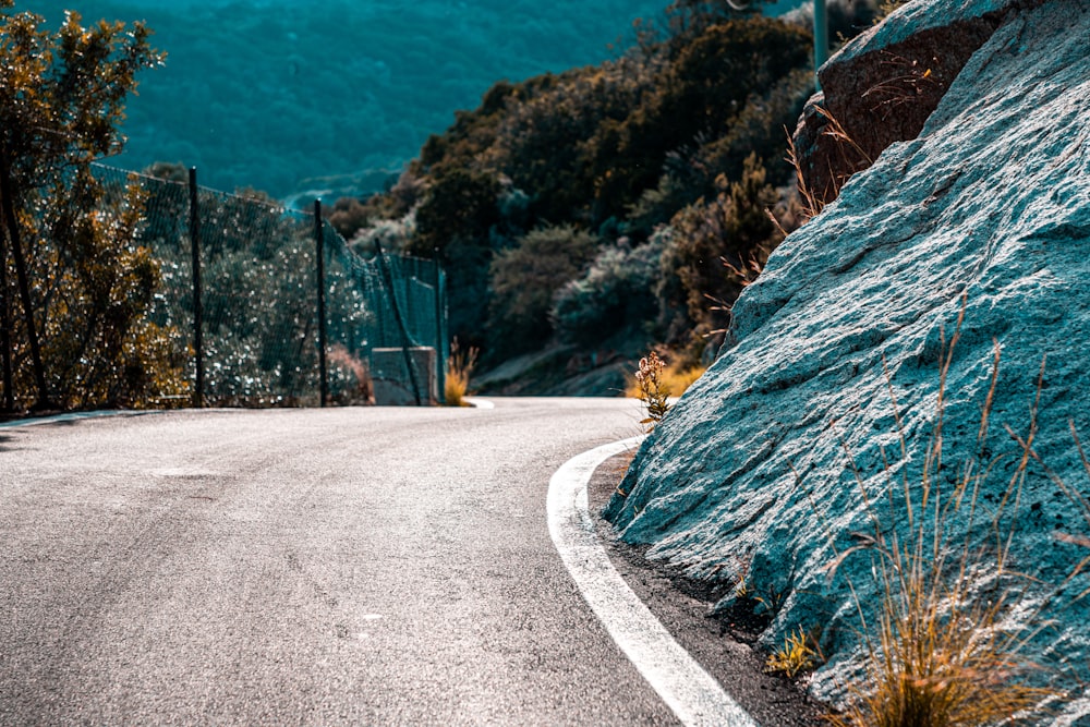 gray concrete road beside green and brown mountain during daytime