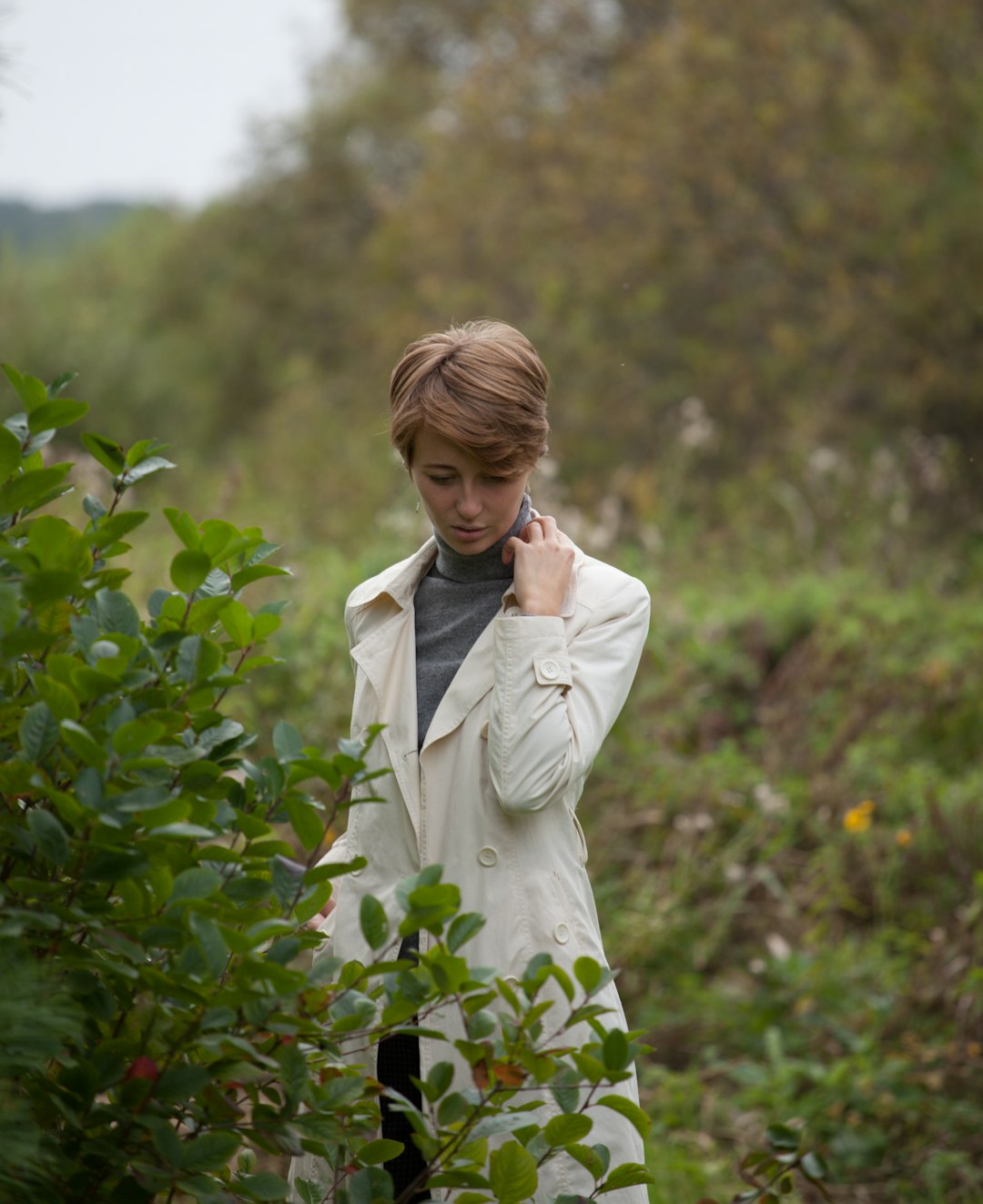 woman in white coat standing near green plants during daytime