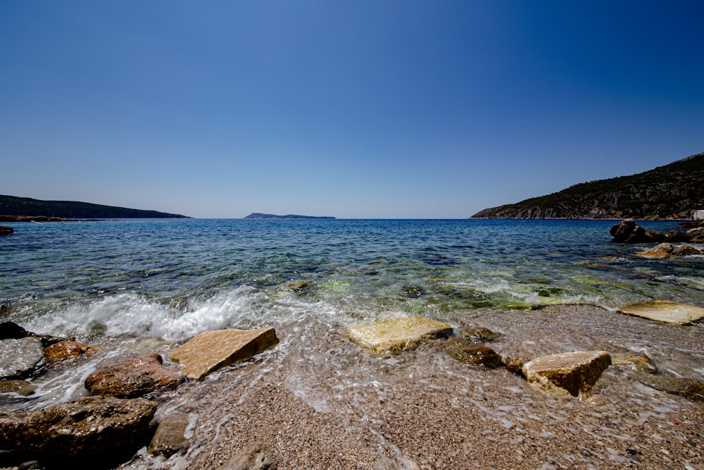 brown rocky shore near body of water under blue sky during daytime