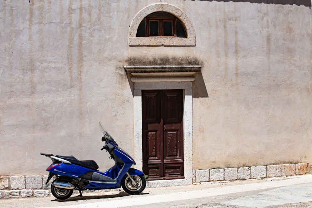 blue motor scooter parked beside brown wooden door
