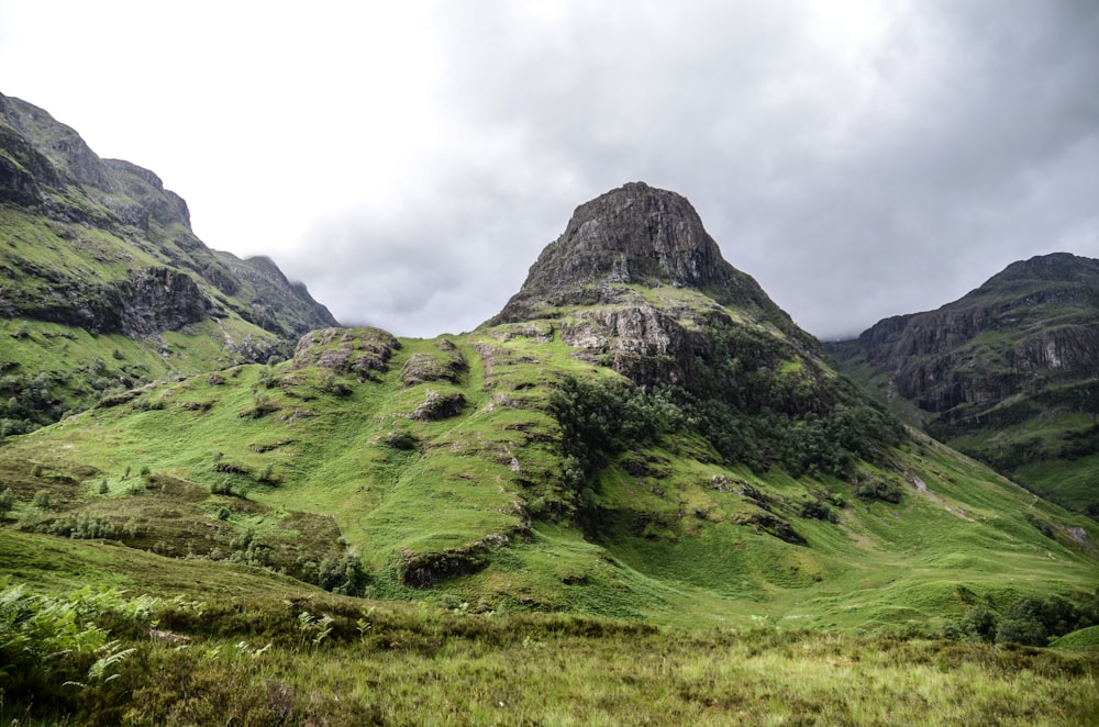 green grass field near mountain under white clouds during daytime