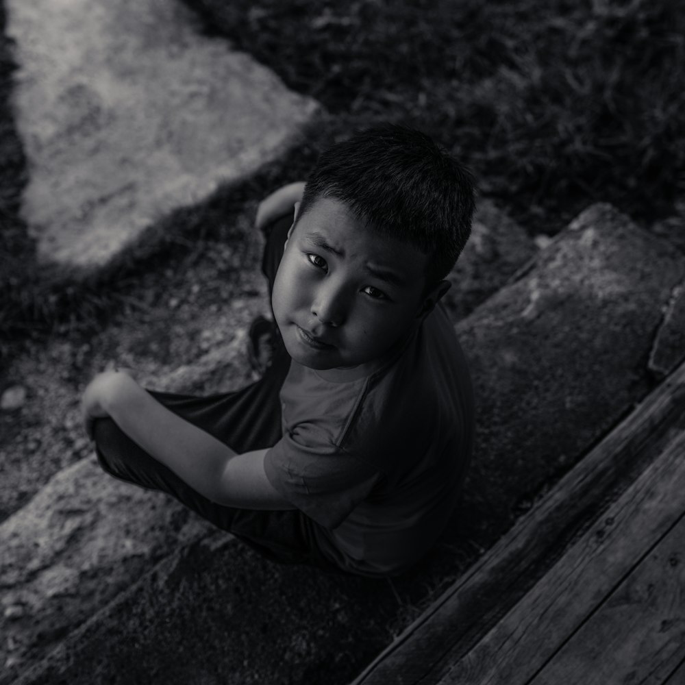 grayscale photo of boy in crew neck t-shirt sitting on wooden bench