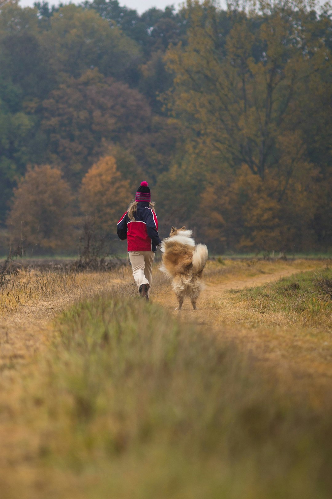 man in red jacket and blue denim jeans walking on brown grass field during daytime