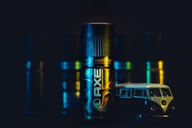 A deodorant can with the brand name 'AXE' is prominently displayed in the foreground against a dark background. The label features swirling designs and the name 'Dark Temptation'. To the right, a small toy van is partially visible, adding a playful element to the composition.