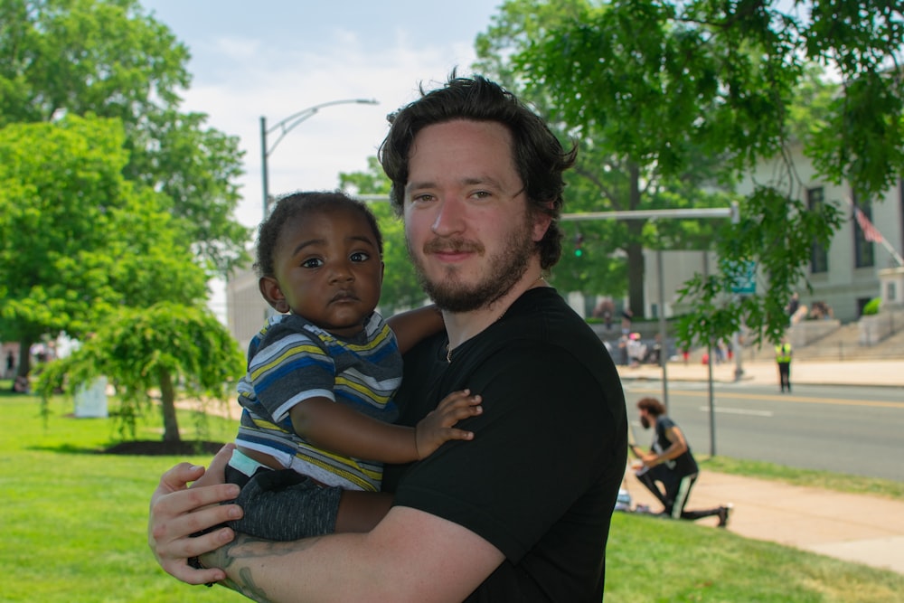 man in black crew neck t-shirt carrying boy in blue white and yellow stripe polo