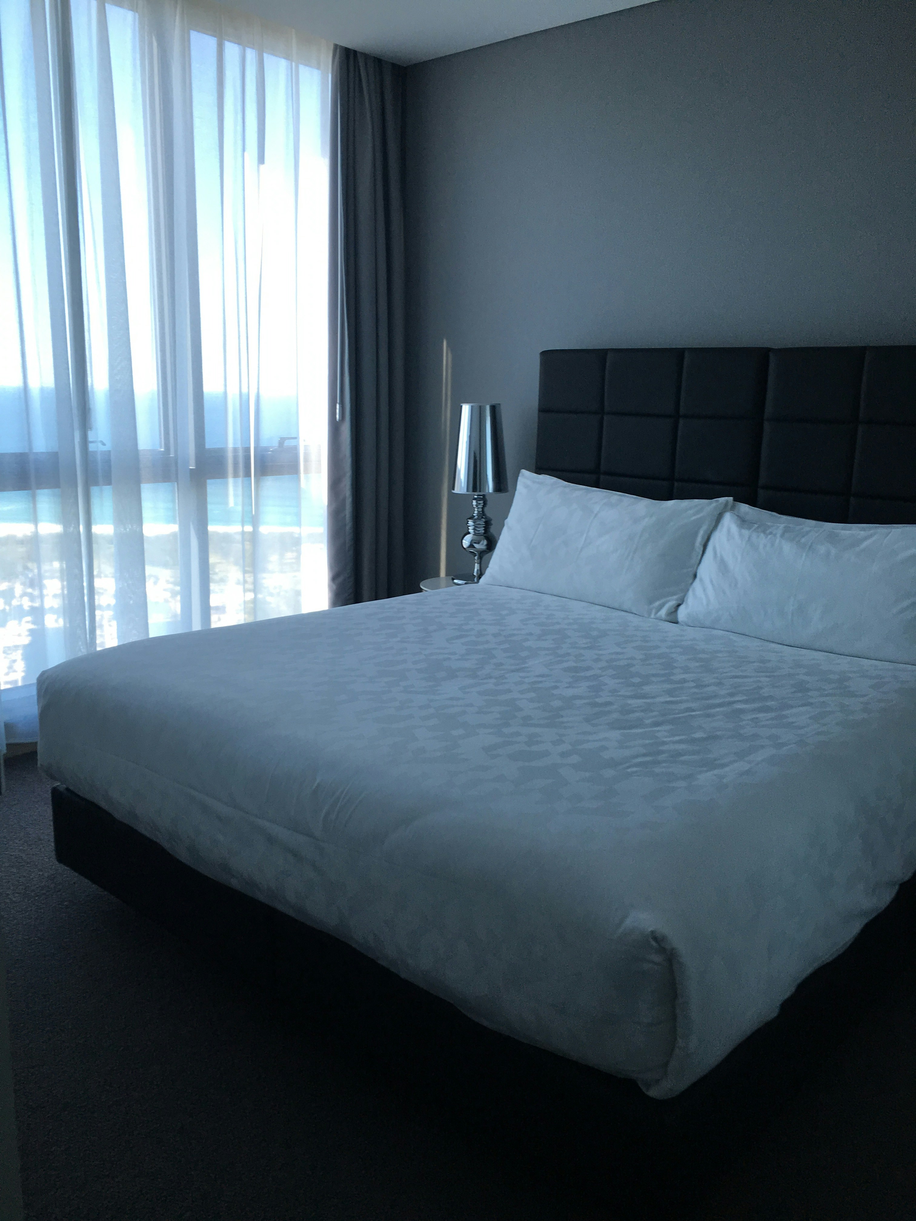Beautifully made hotel-style bed with crisp white linen in a bright, airy Cape Town Airbnb rental room, natural light streaming through windows