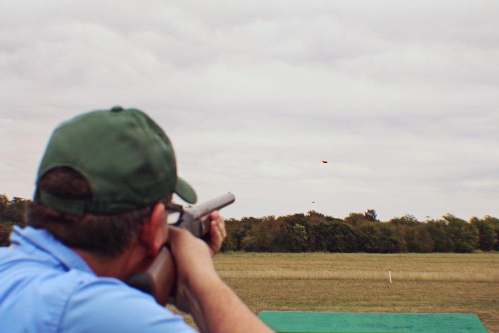 man in blue shirt and green cap holding black rifle