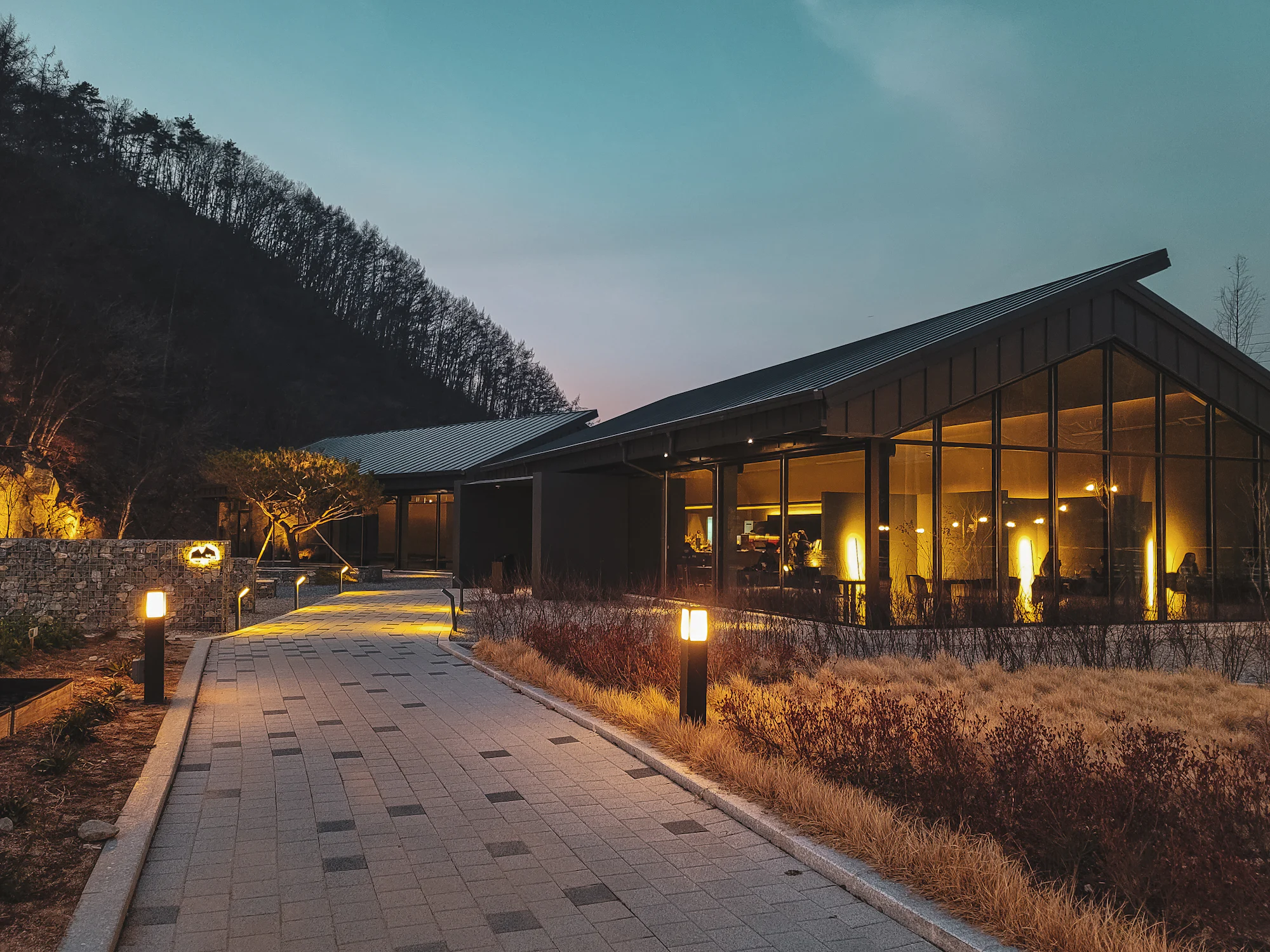 The arrival pavilion glowing at dusk beneath a forested ridge