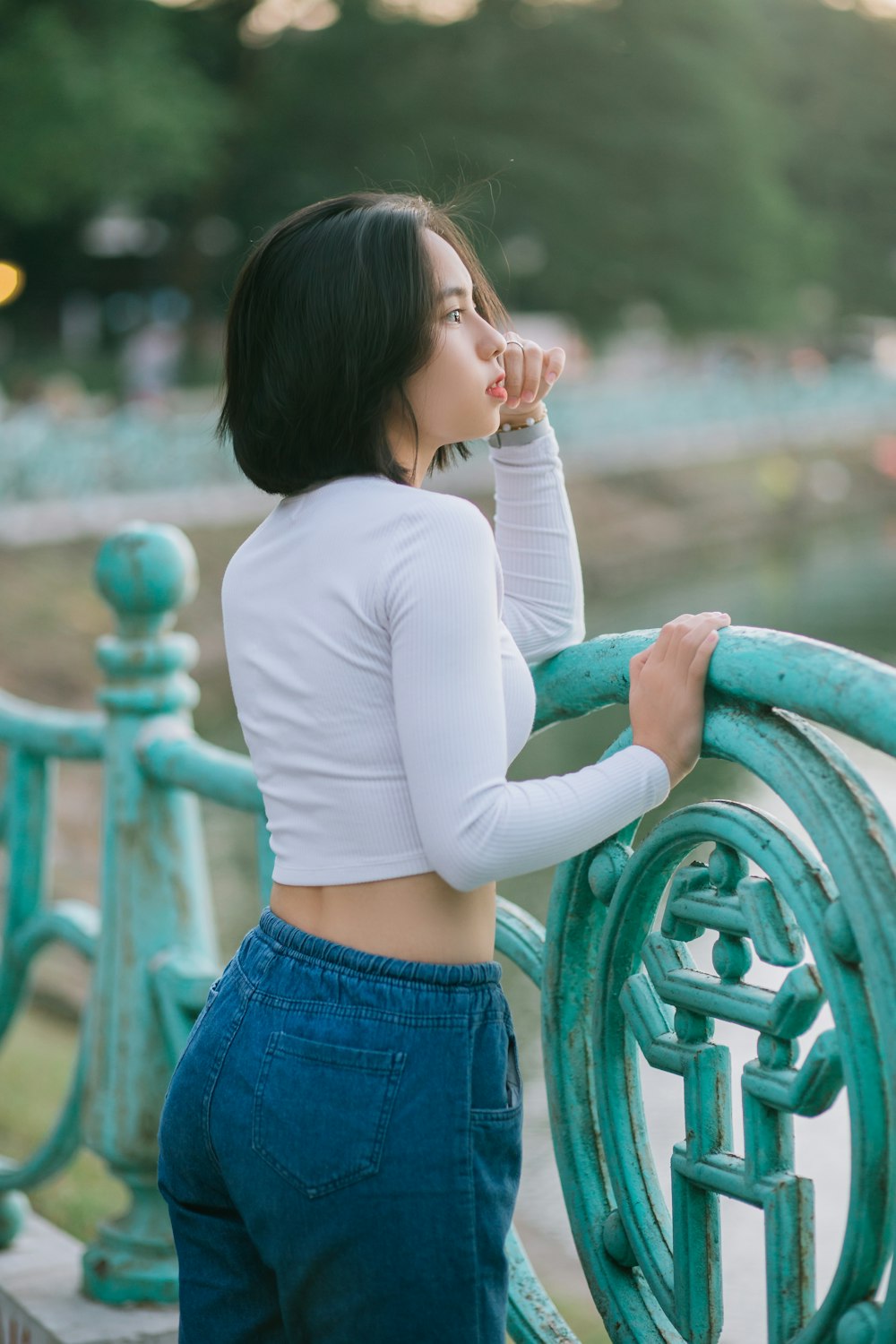 woman in white long sleeve shirt and blue denim shorts leaning on green metal railings during