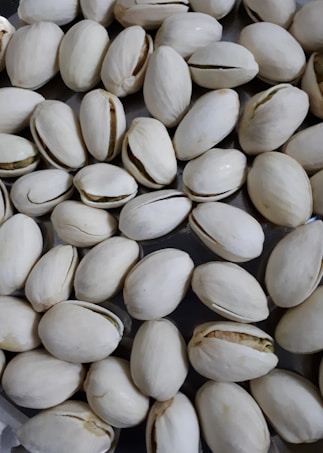 A pile of pistachio nuts with their shells mostly closed, scattered in a slightly overlapping pattern.