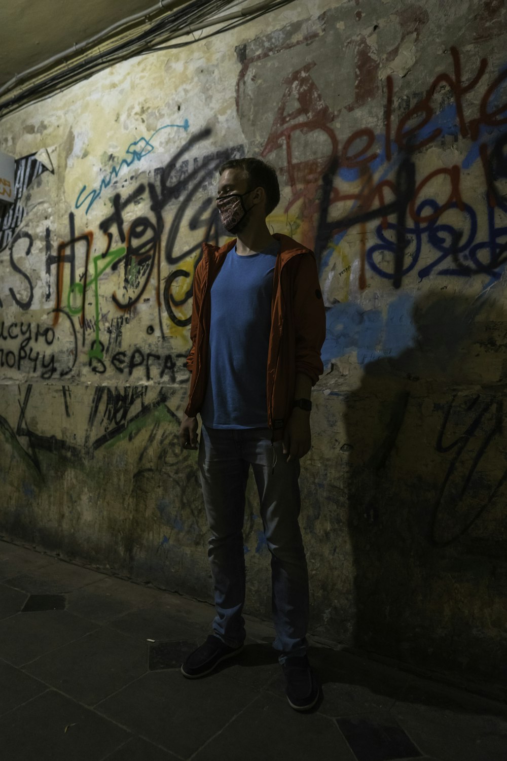 mujer en chaqueta roja y azul de pie junto a la pared con graffiti