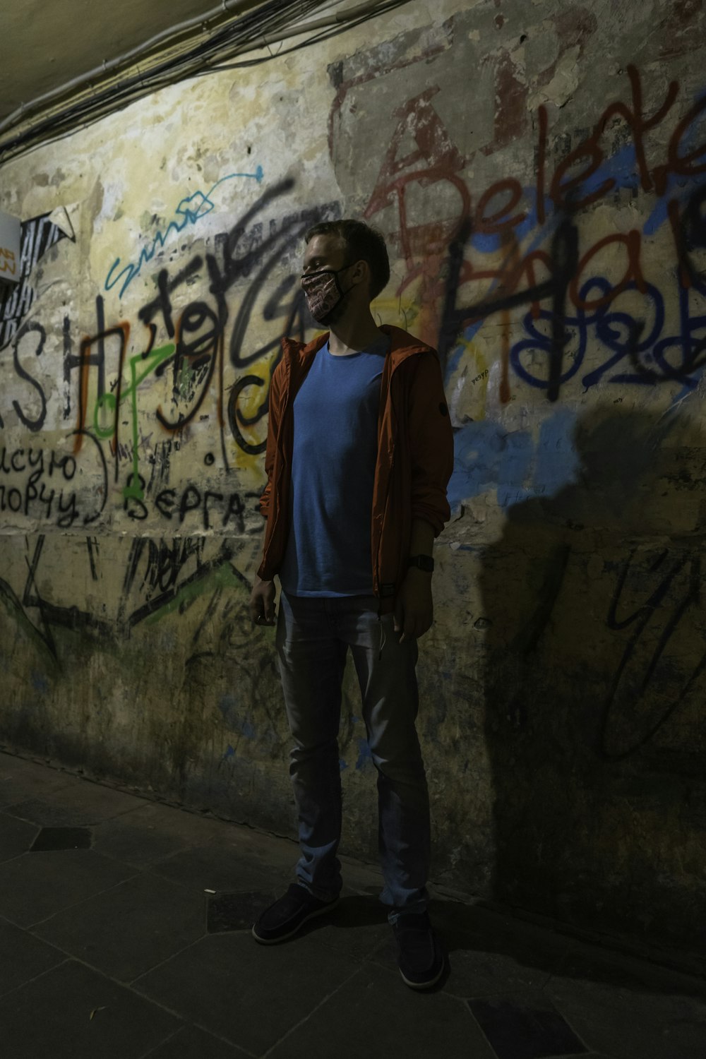 woman in red and blue jacket standing beside wall with graffiti
