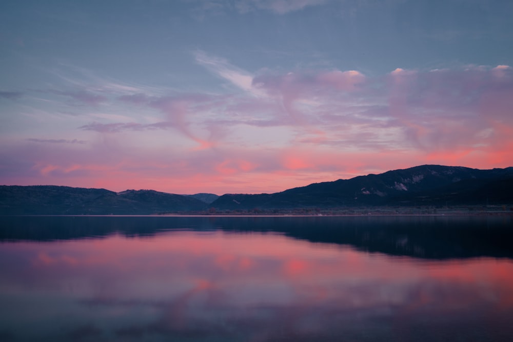 body of water near mountain under cloudy sky during daytime